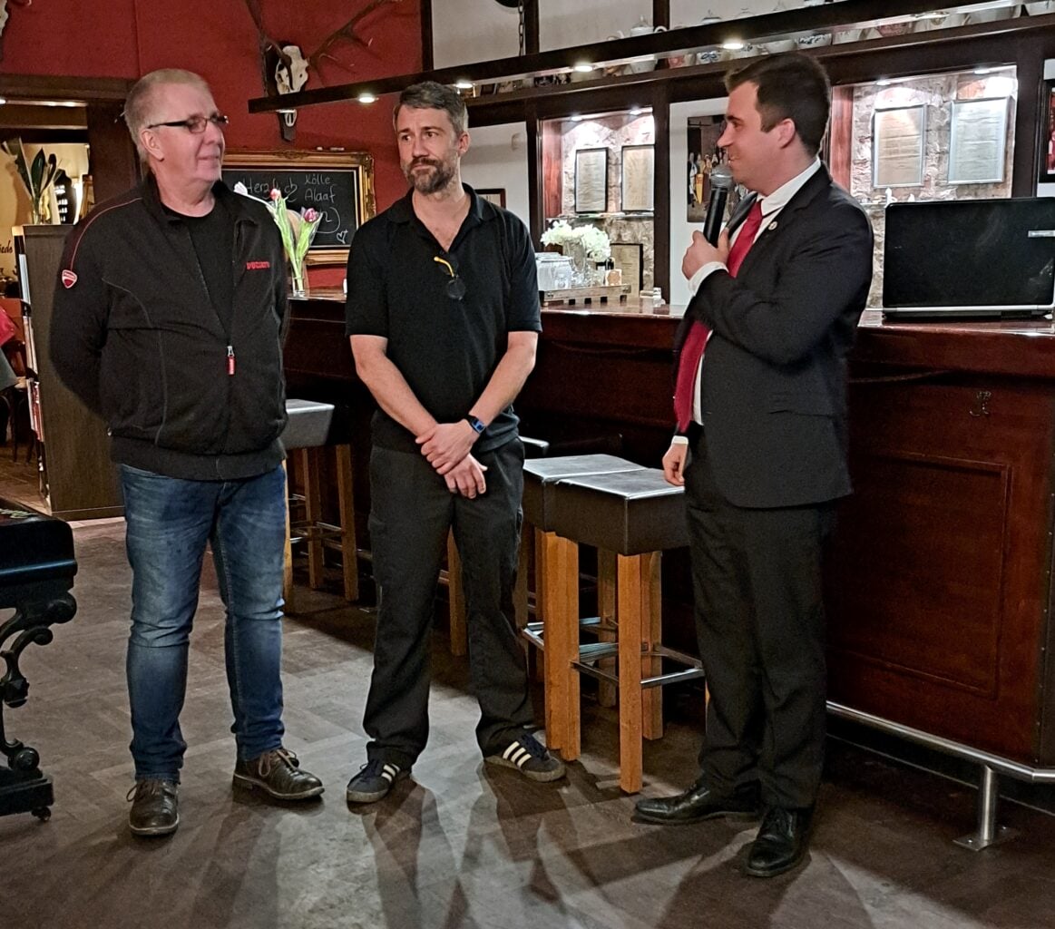 Drei Männer stehen vor einer Bar und besprechen Pläne für die Fischessen-Veranstaltung im Motto 2023/24.