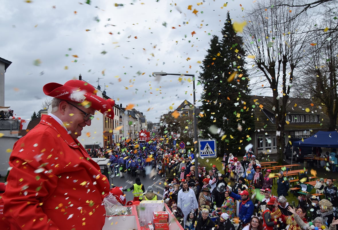 Ein Mann im roten Anzug wirft während der ROSENSONNTAGSZUG-Veranstaltung in PORZER am 19.02.2023 Konfetti auf eine Menschenmenge.