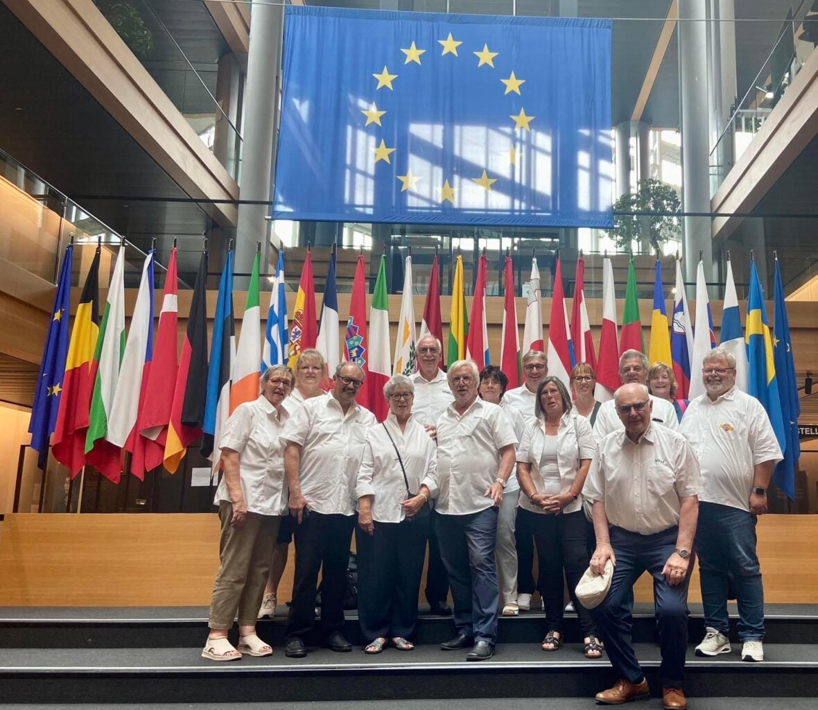 Eine Gruppe von Menschen posiert vor EU-Flaggen, die die Europastadt Straßburg repräsentieren, und umarmt den Senat, umgeben von einem bezaubernden blau-weißen Funke Wahn.