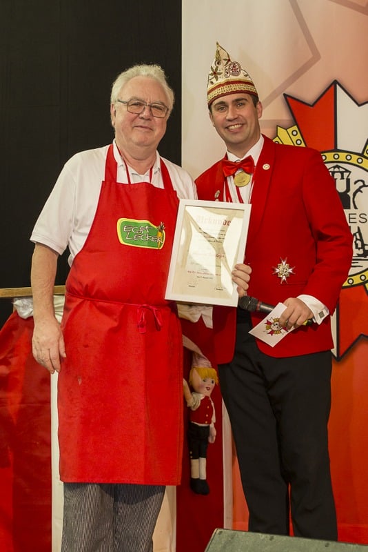 Zwei Männer in roten Schürzen, Jakob-Engelshalle und Sessionseröffnung, stehen nebeneinander.